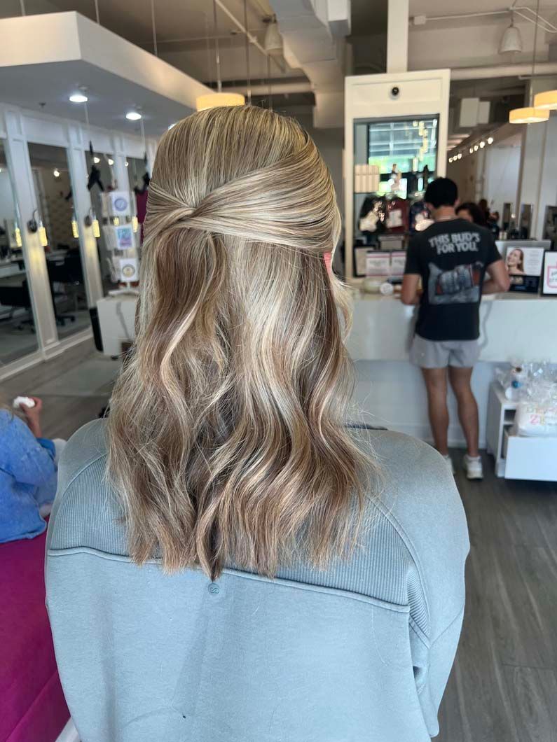 Woman with wavy, blonde hair in a half-up style stands in a hair salon.