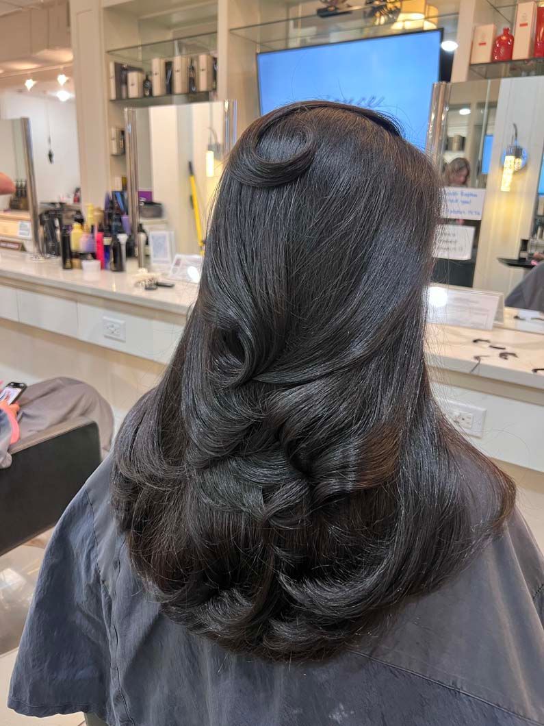 Dark hair styled in layers and curls, viewed from the back in a salon.