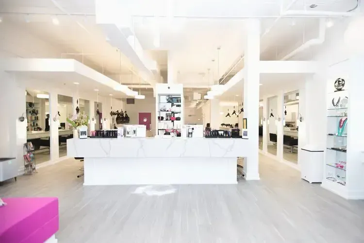 Brightly lit white hair salon interior with mirrors, stations, and reception desk.