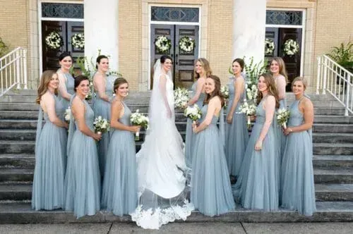 Bride with bridesmaids in blue dresses, posing on steps of a building with columns.