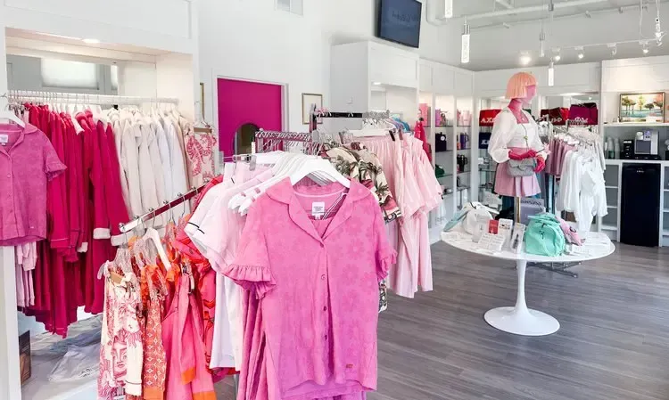 Clothing store interior with racks of pink and white clothing. A mannequin and display table are also present.