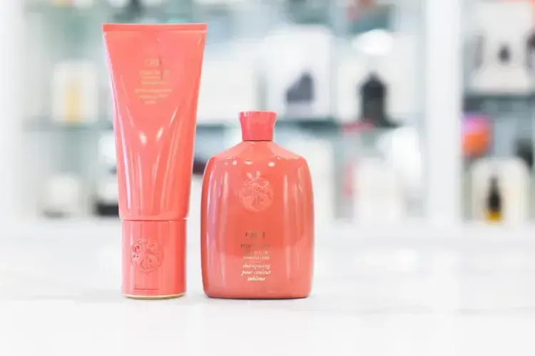 Two coral-colored cosmetic containers on a white surface, one tall tube and a rounded bottle.