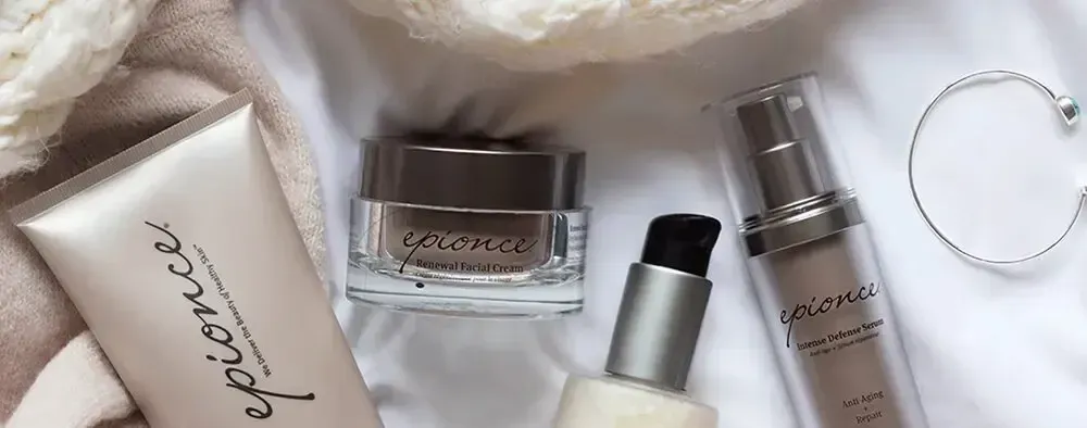 Skincare products including tubes and bottles, with a bracelet, on a beige surface.