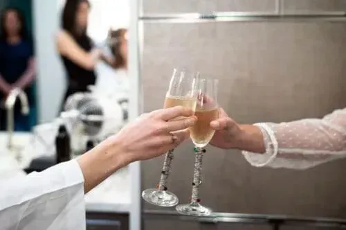Two people toasting champagne flutes. Shiny glasses, kitchen setting.