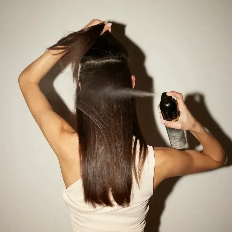 Woman spraying hair with hairspray, back view, indoors.