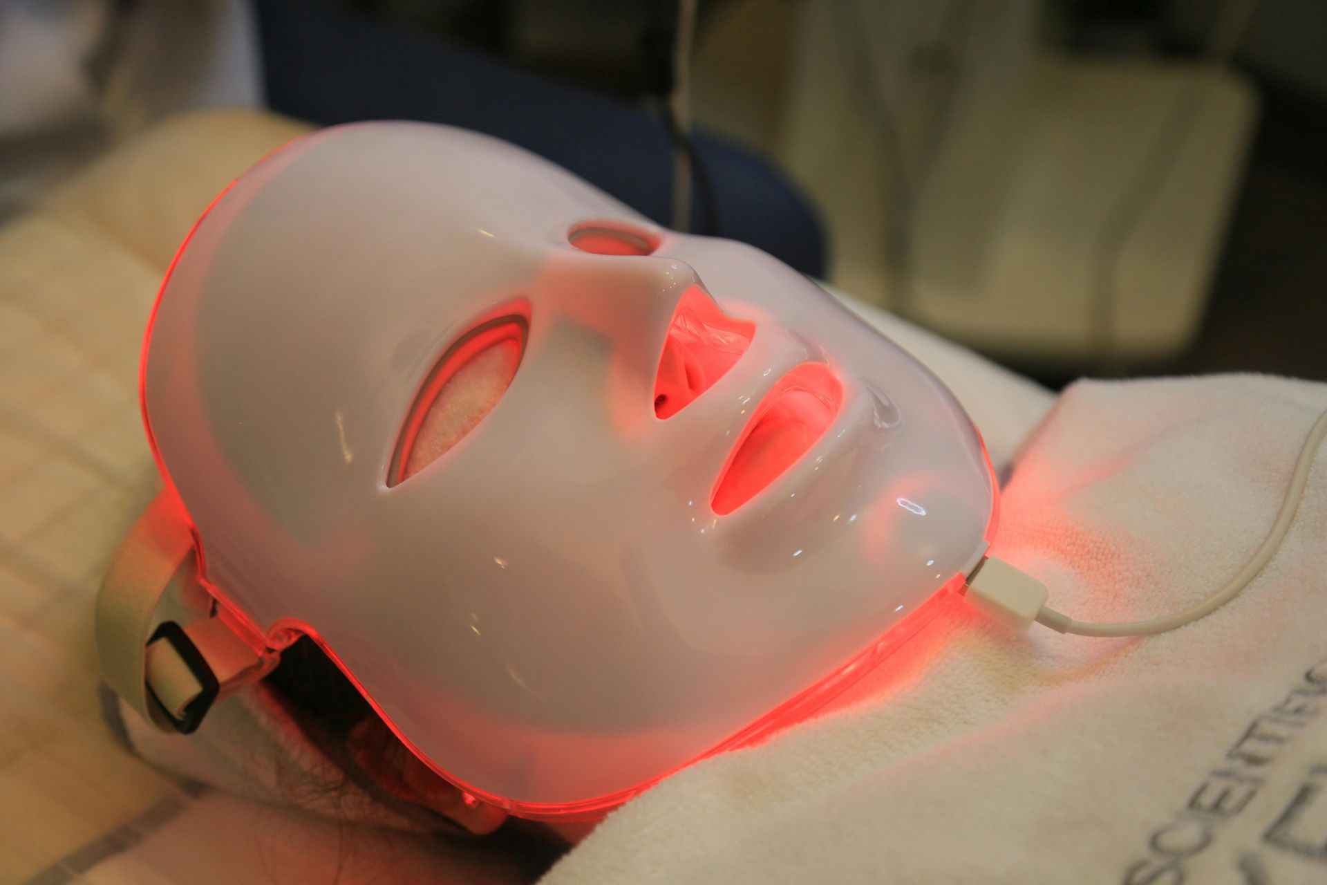 White LED light therapy mask on a person's face, emitting red light in a spa setting.