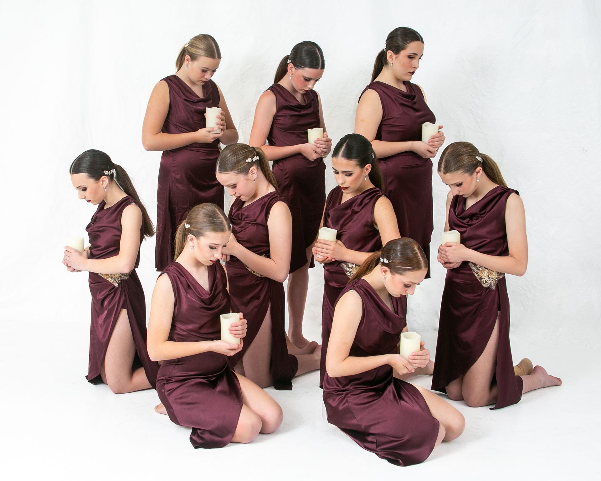 A group of women in purple dresses are kneeling down and holding candles.