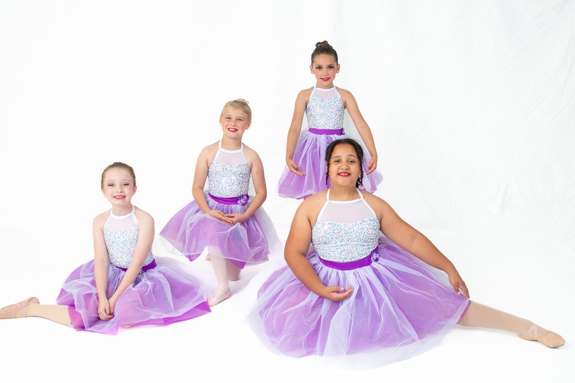 A group of young girls in purple tutus are posing for a picture.