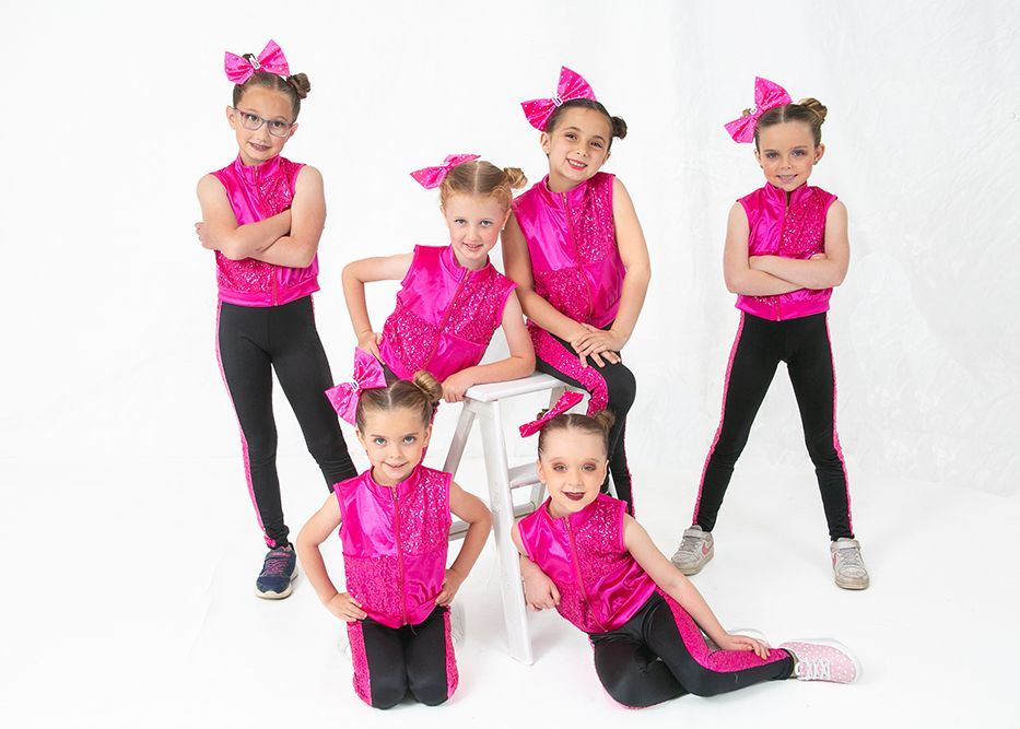 A group of young girls in pink and black outfits are posing for a picture.