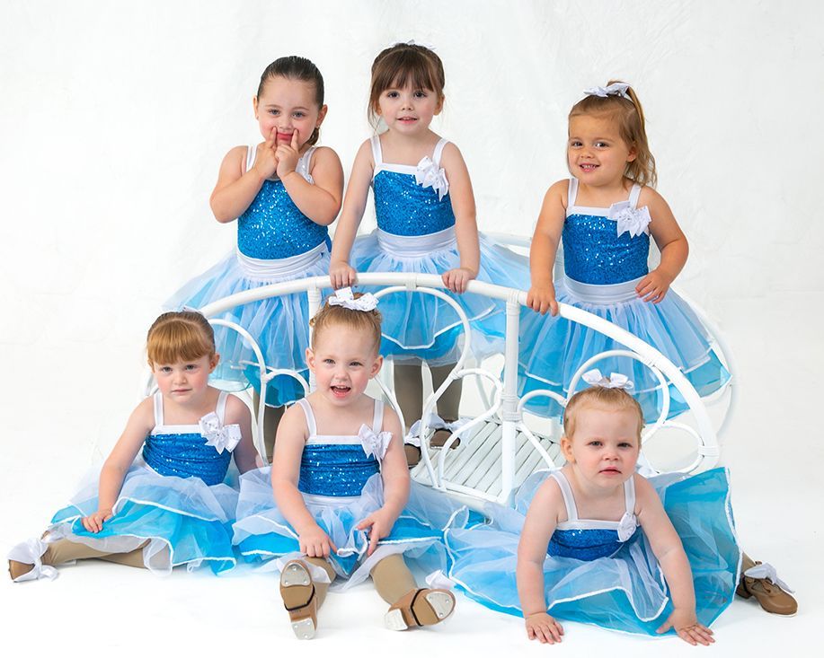 A group of little girls in blue and white dresses are posing for a picture.