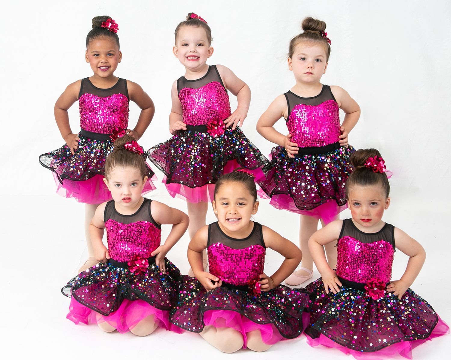 A group of young girls in pink and black sequined dresses are posing for a picture.