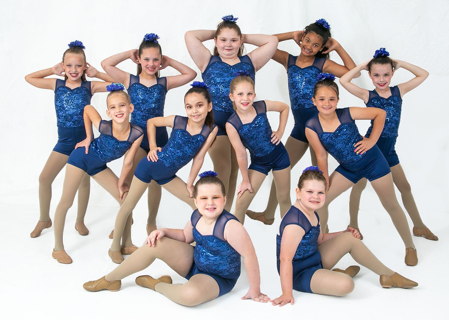 A group of young girls in blue leotards are posing for a picture.