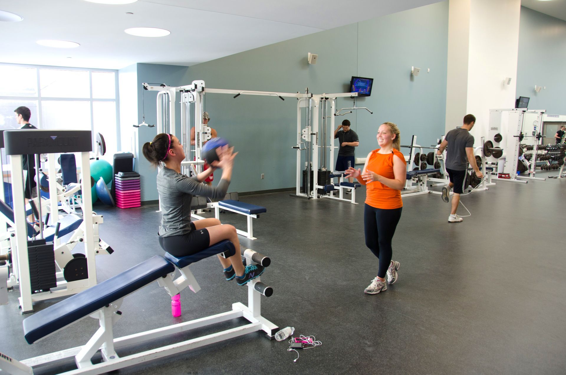 A woman is sitting on a bench in a gym talking to another woman.