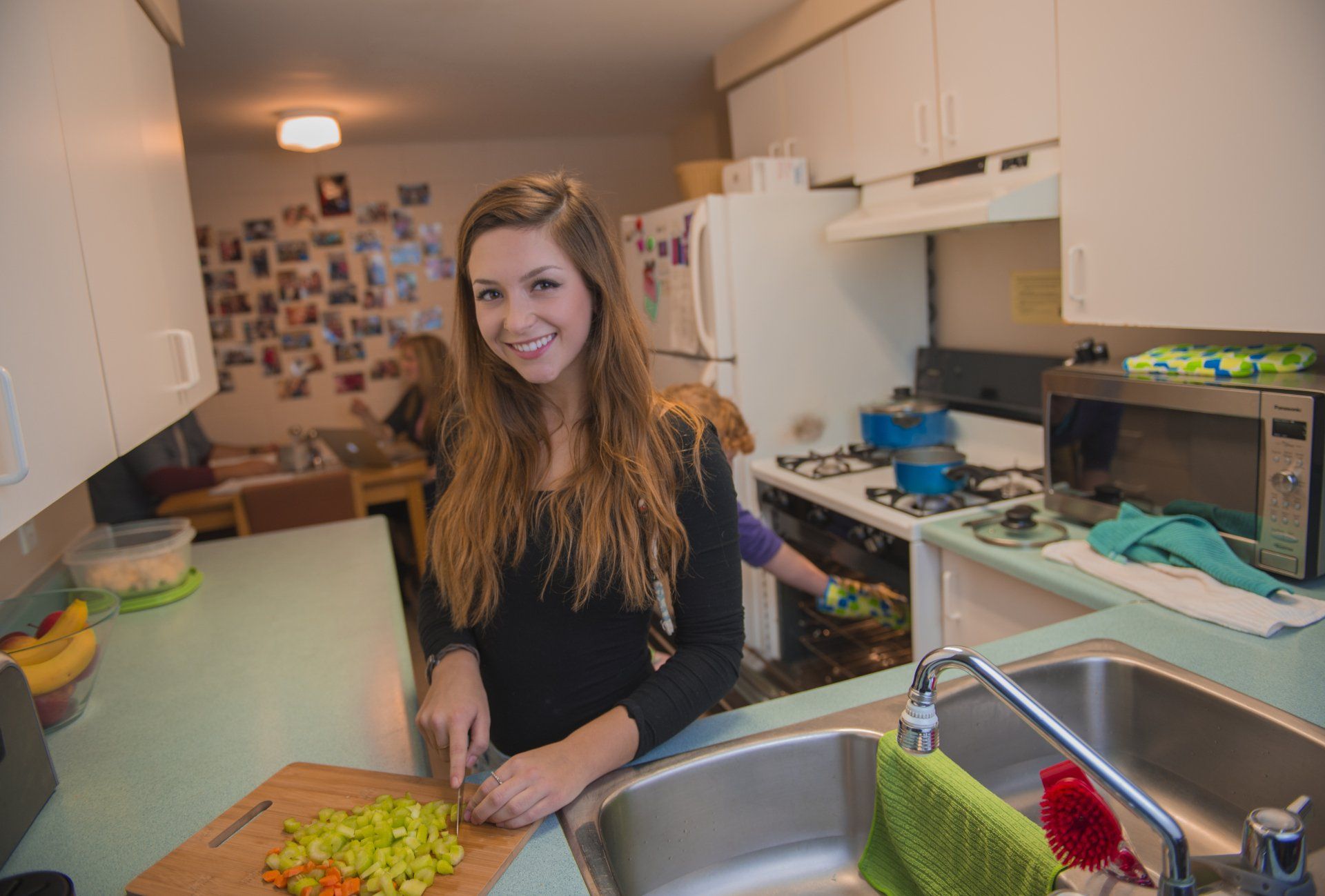 A woman is cutting vegetables on a cutting board in a kitchen.