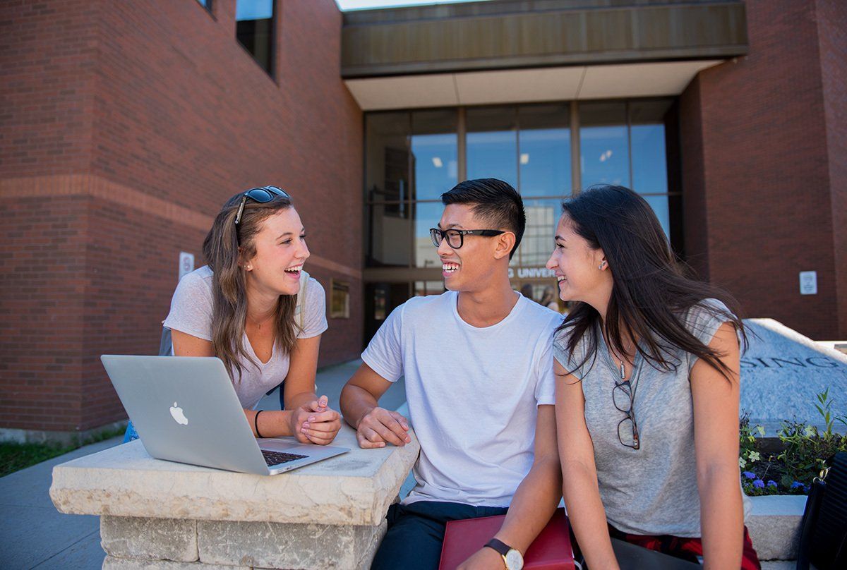 A group of people are sitting on a bench with a laptop.