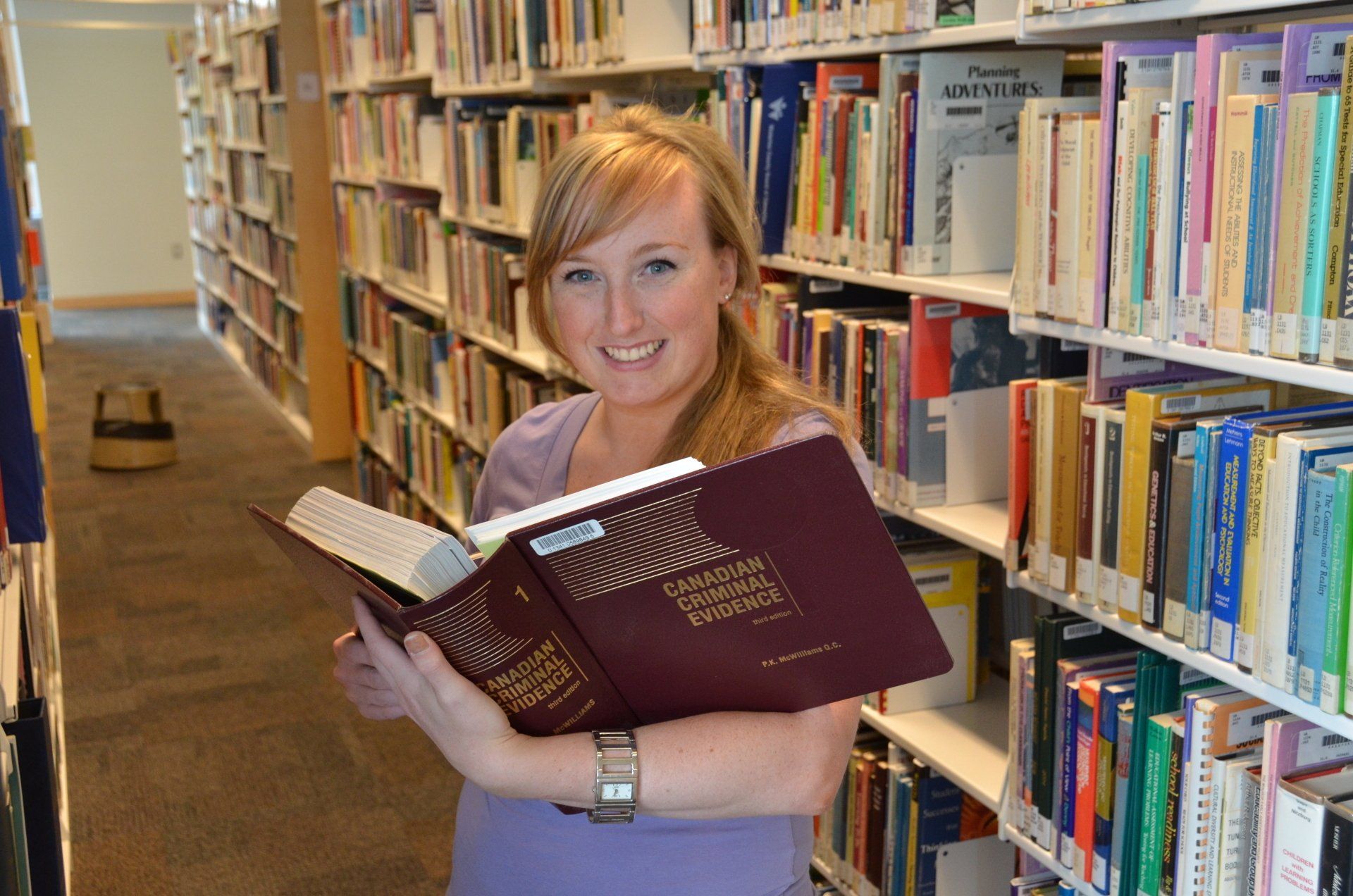 A student in the Harris Learning Library holding a book titled Canadian Criminal Evidence