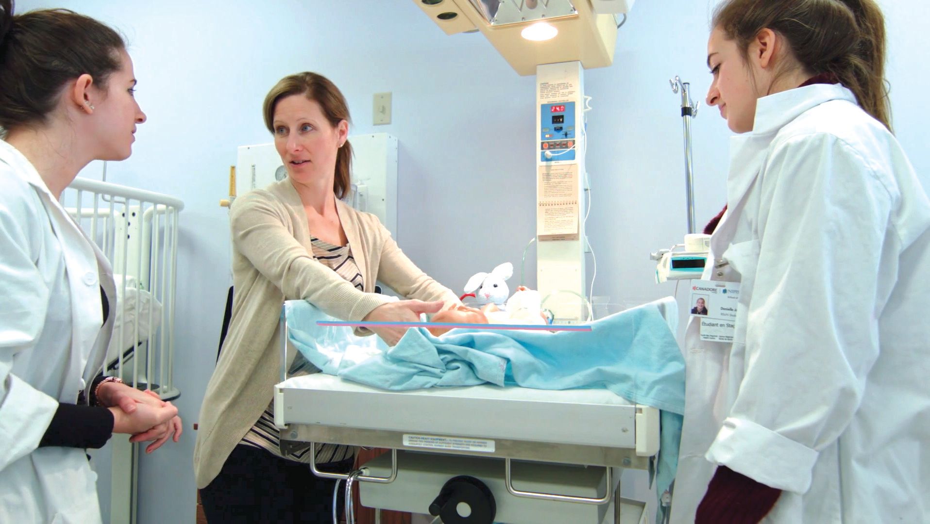 A group of women are standing around a baby in a hospital room.
