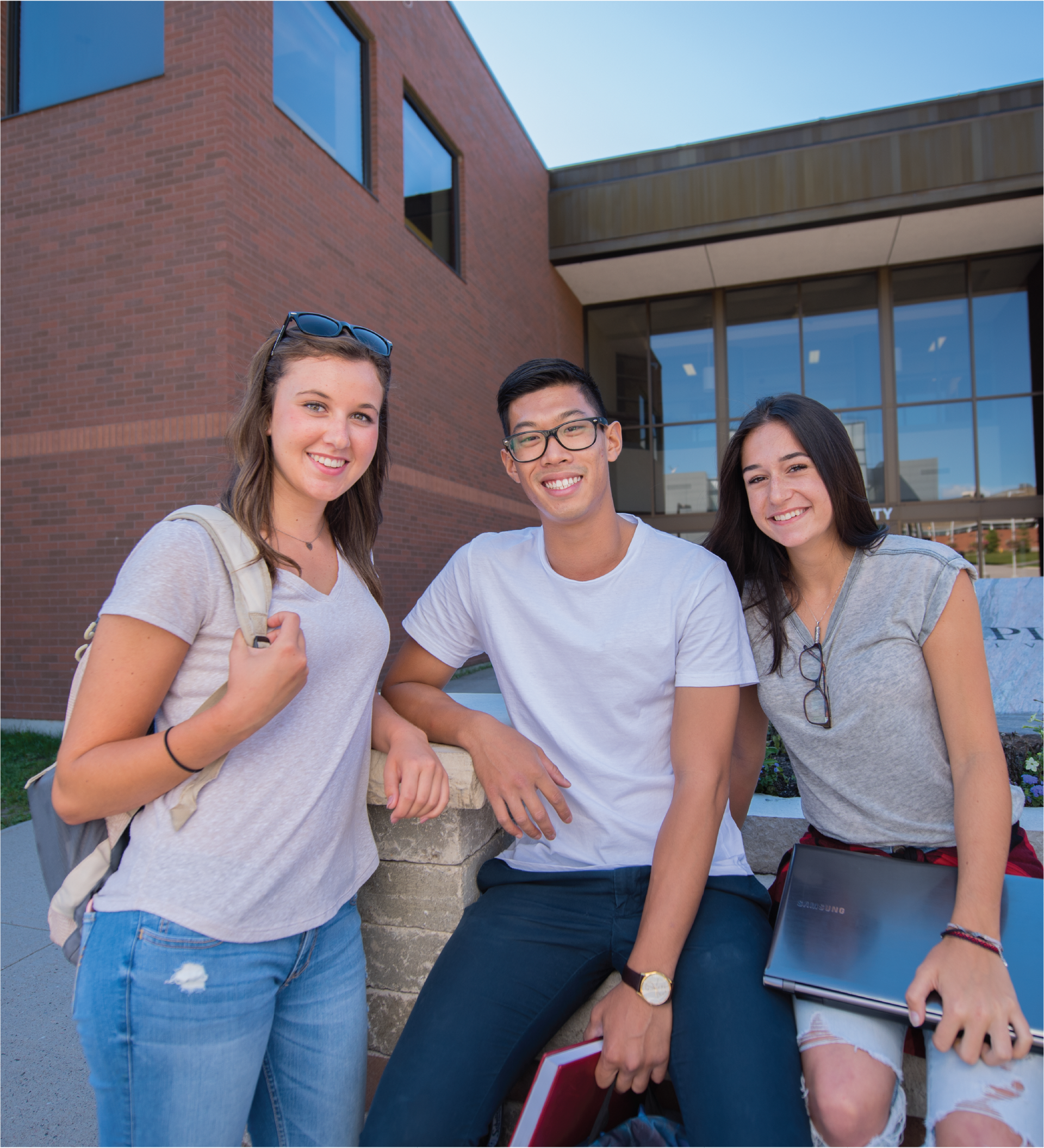 3 students posing and smiling in front of the main entrance