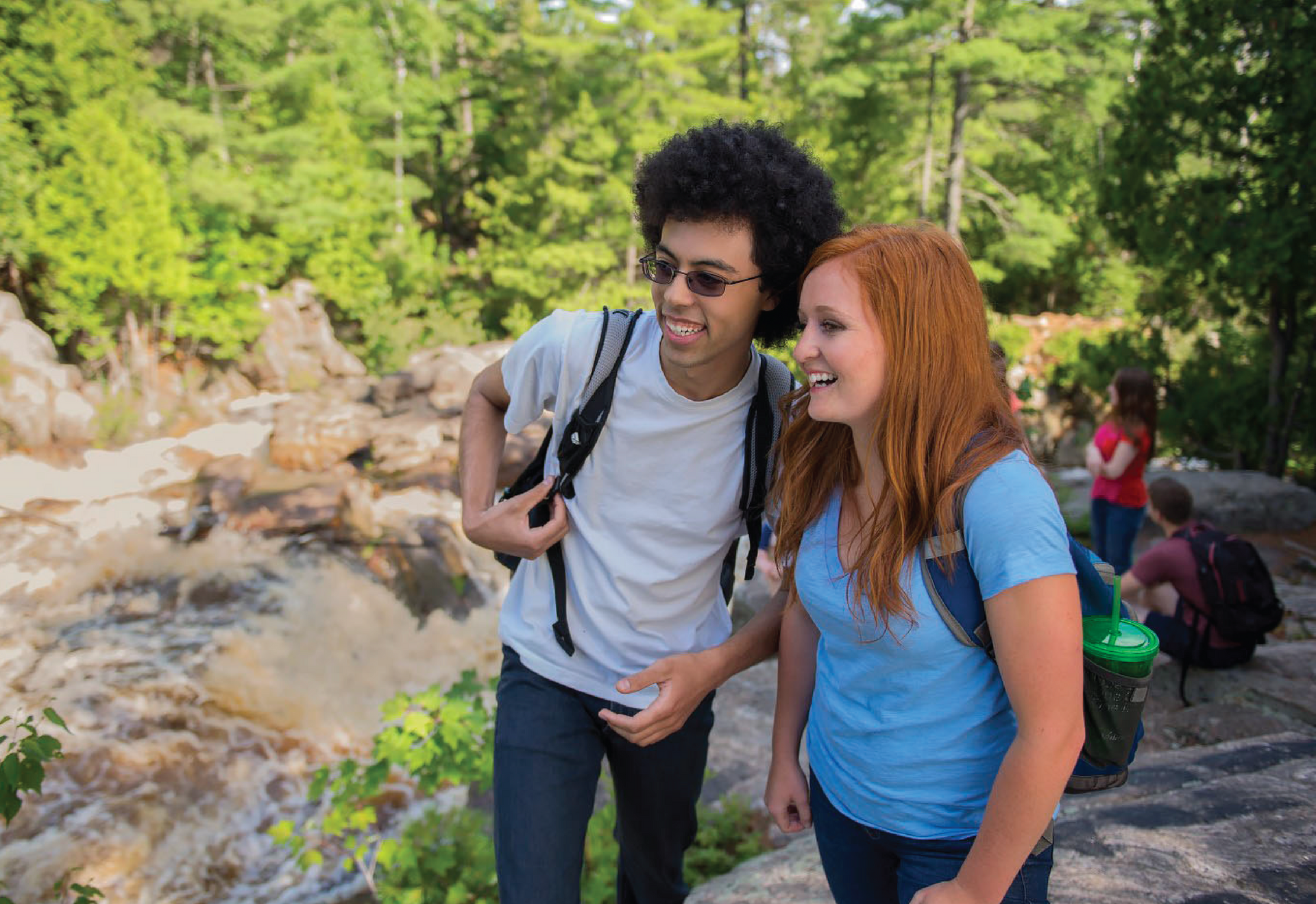 2 students standing on top of a rock looking out at the waterfall