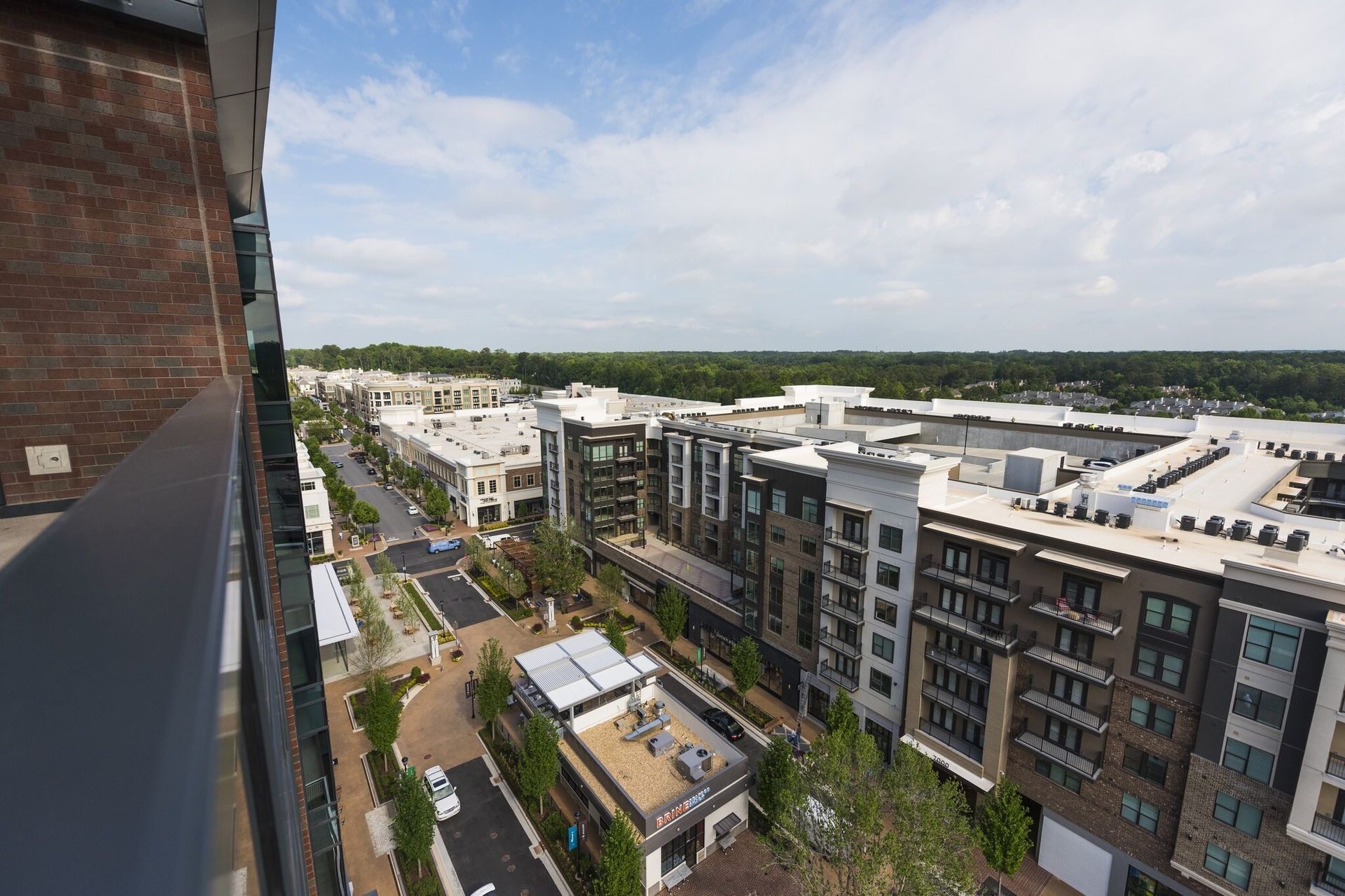 View of modern buildings, street with cars, trees, and a blue sky. Brick building edge in the foreground.