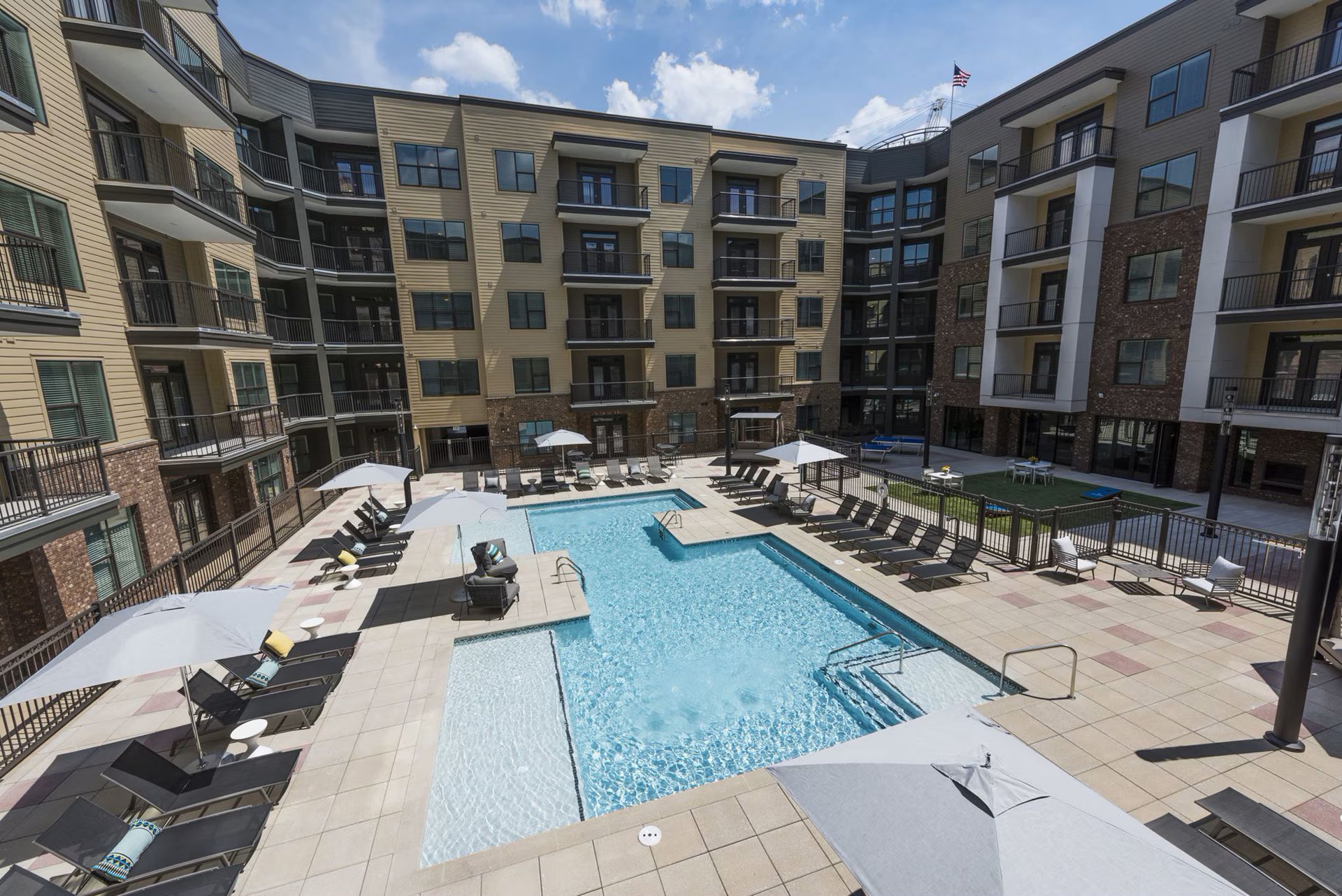 Courtyard with pool surrounded by multi-story apartment buildings on a sunny day.