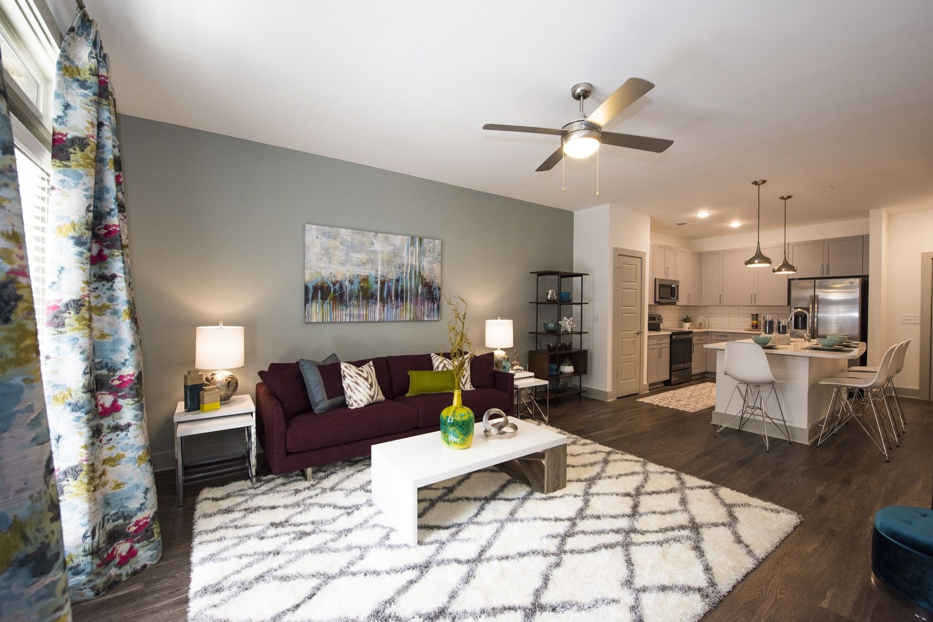 Living room with burgundy couch, white rug, and open kitchen; gray walls, wood floors.