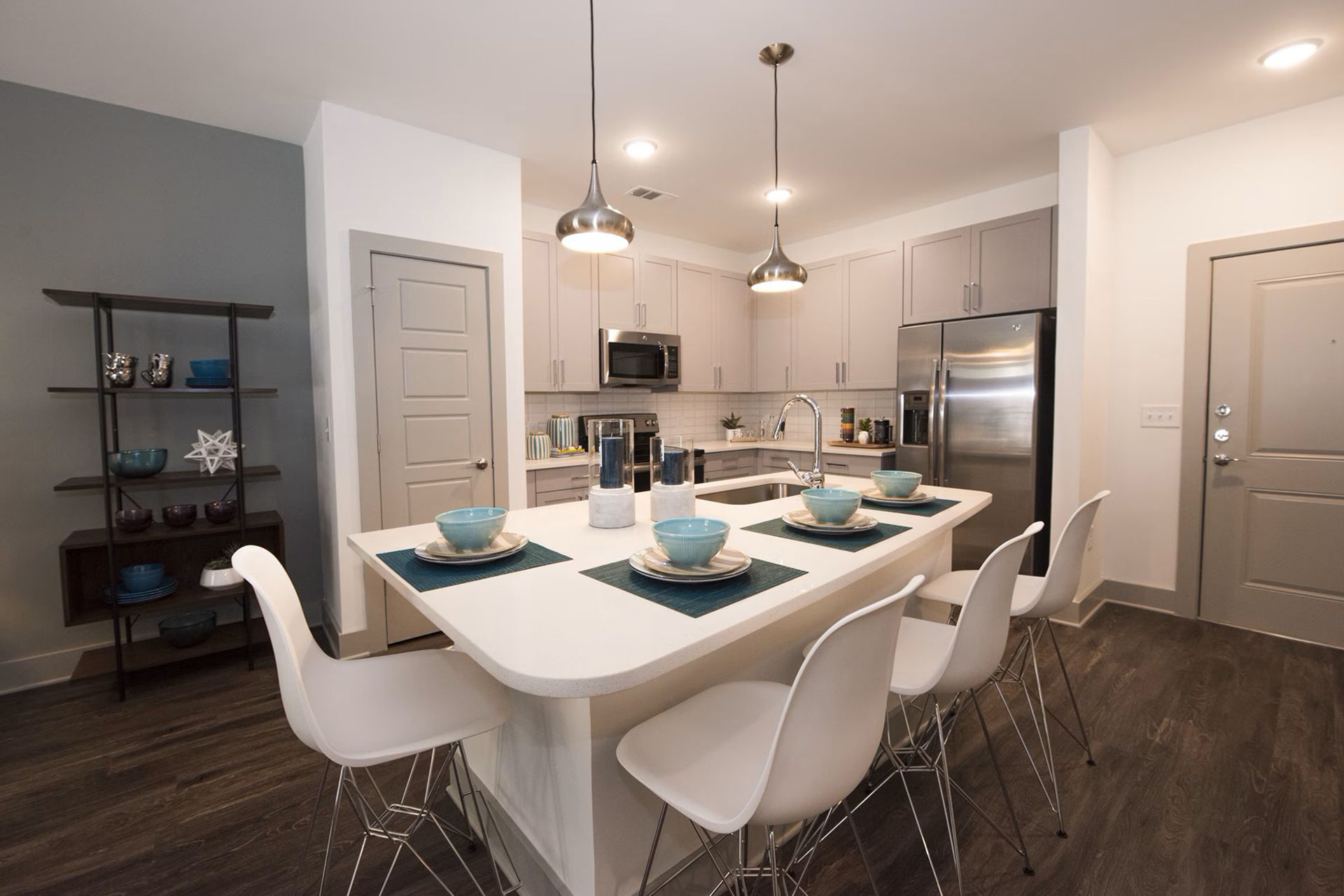 Modern kitchen with island, white chairs, stainless steel appliances, light wood cabinets, and gray walls.