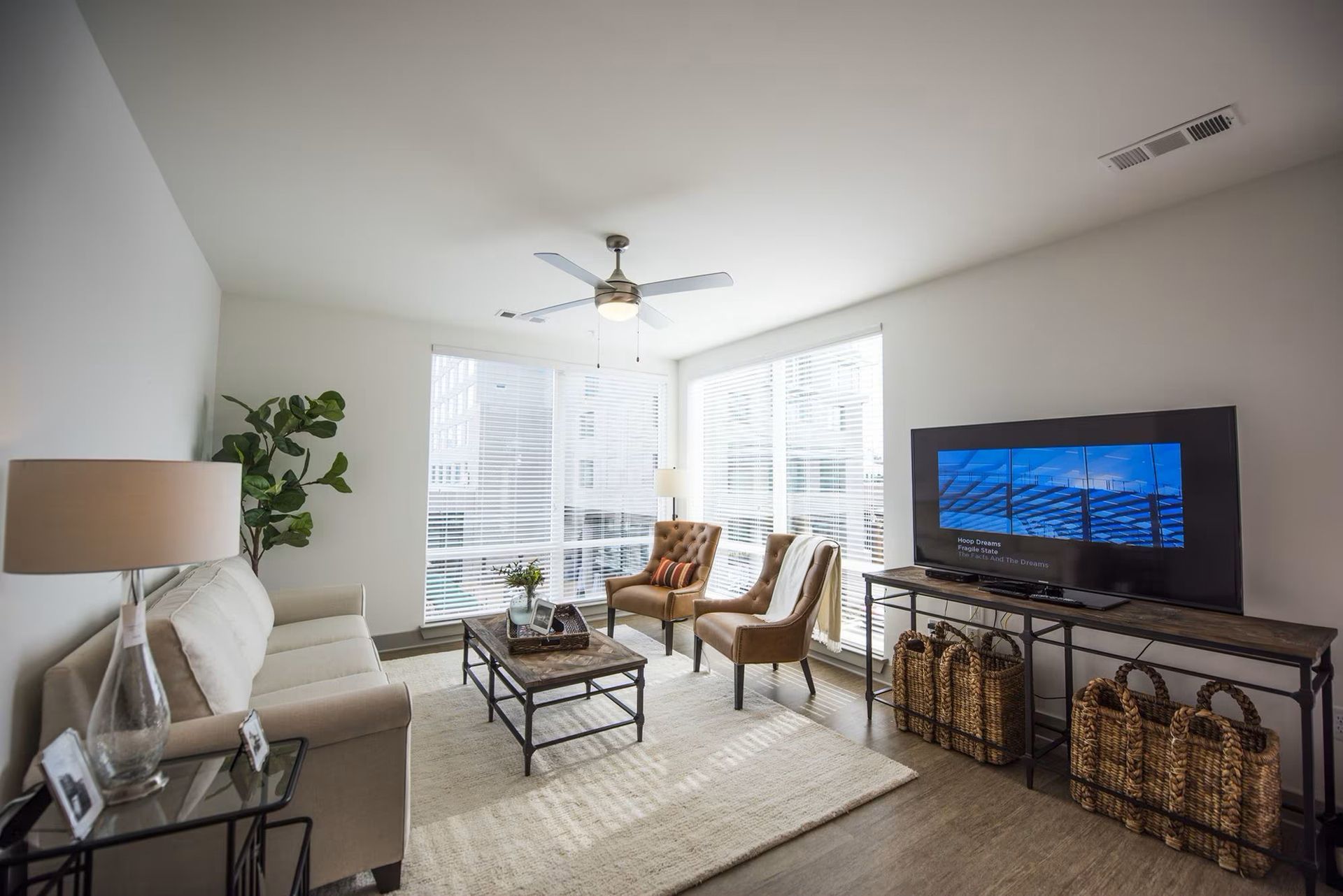 Modern living room with neutral tones, large windows, and a television.