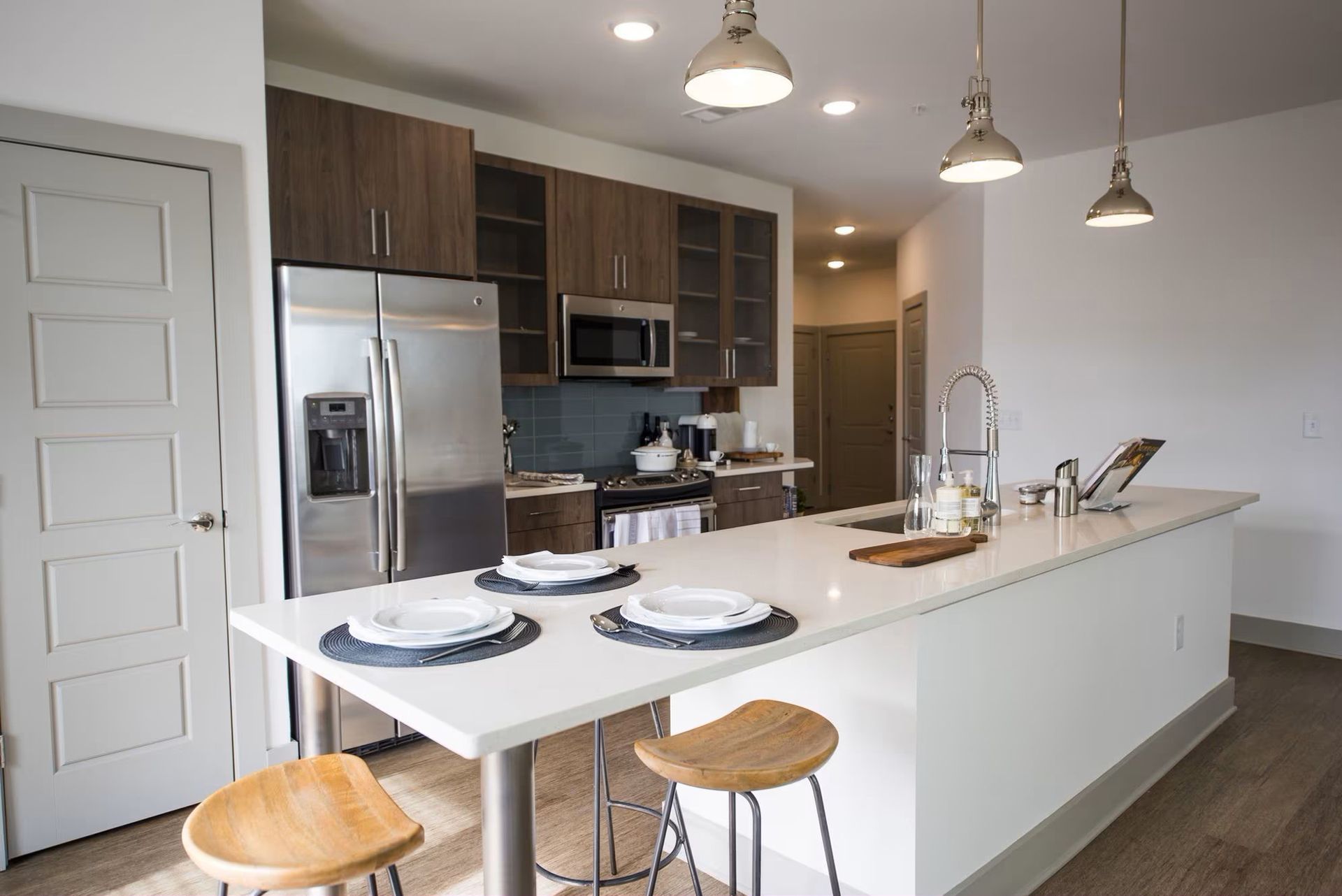 Modern kitchen with island, stainless steel appliances, wood cabinets, and three pendant lights.
