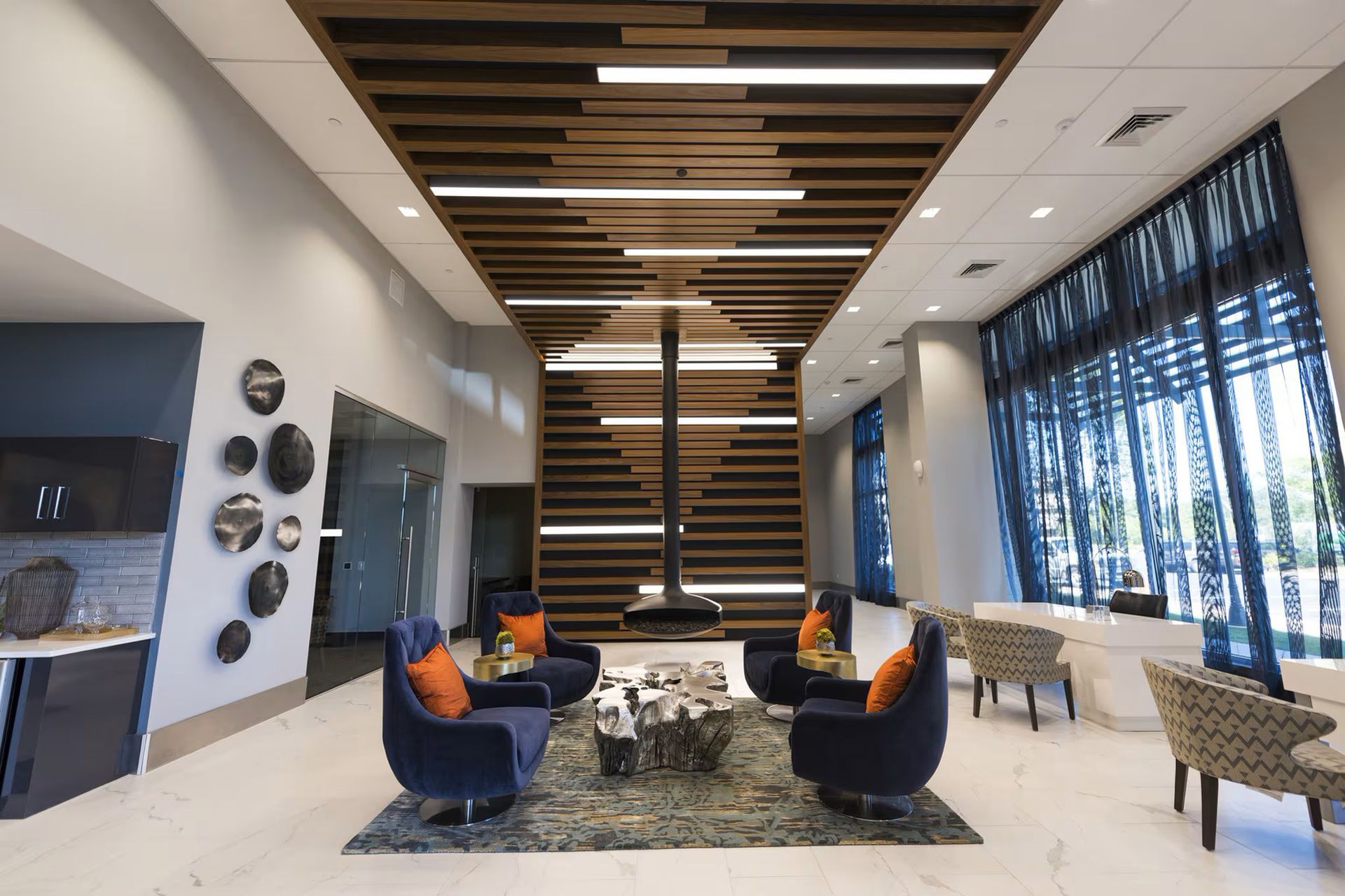 Lounge area with blue armchairs, a central fireplace, and wood ceiling design; bright, airy, and modern.