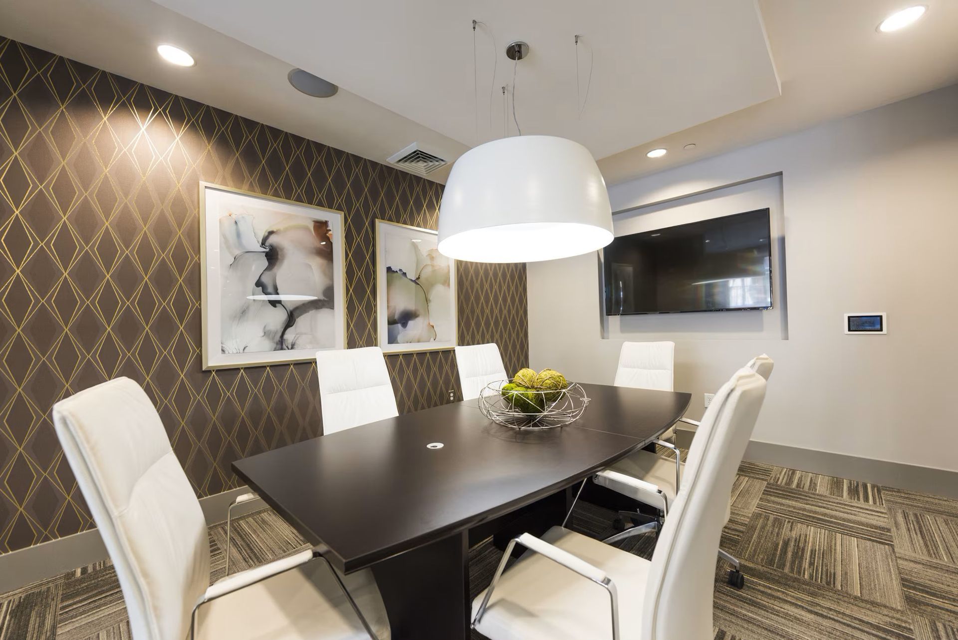 Meeting room with a dark wood table, white chairs, artwork, and a large light fixture.