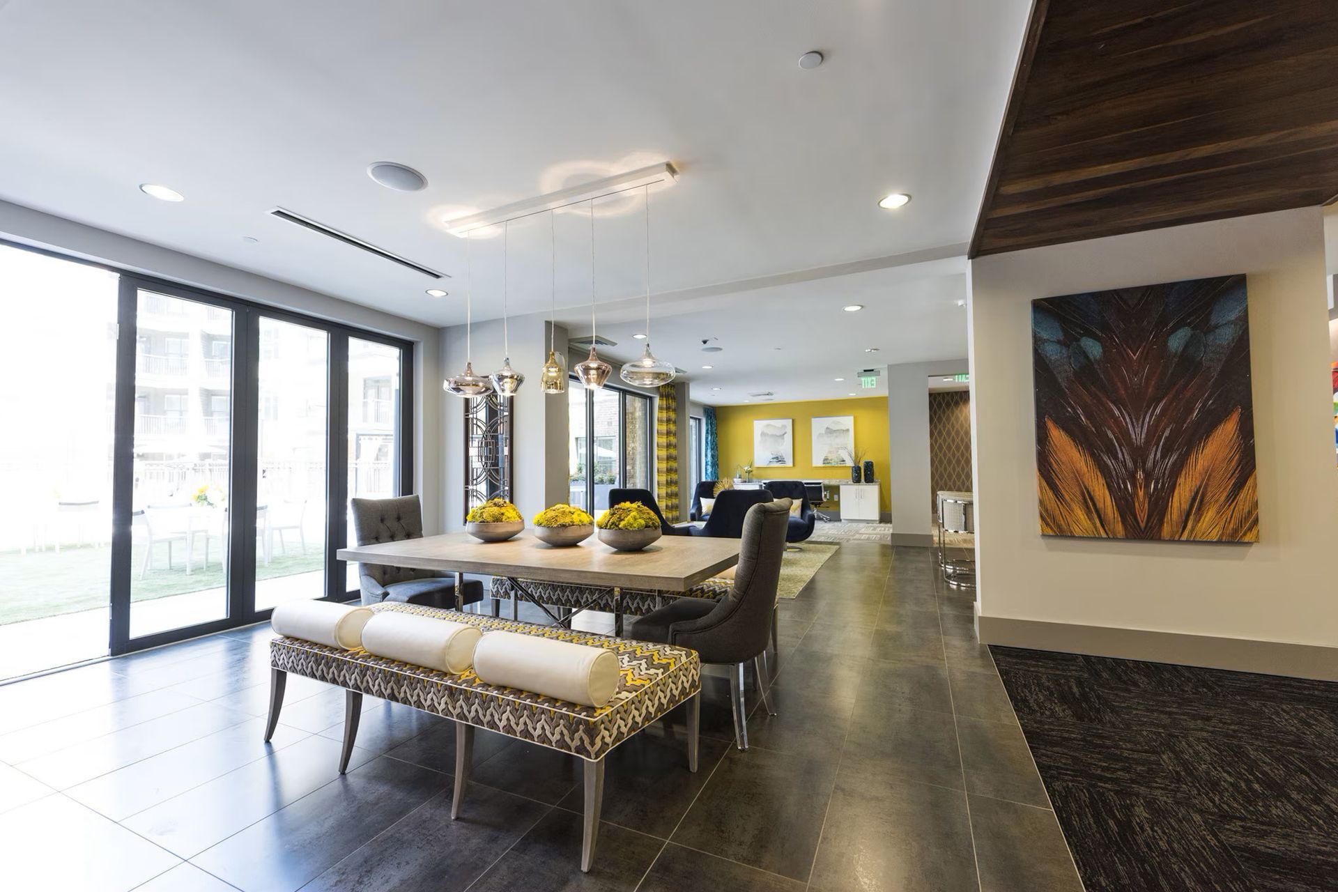Spacious modern dining area with a long table, seating, and large windows overlooking a green space.
