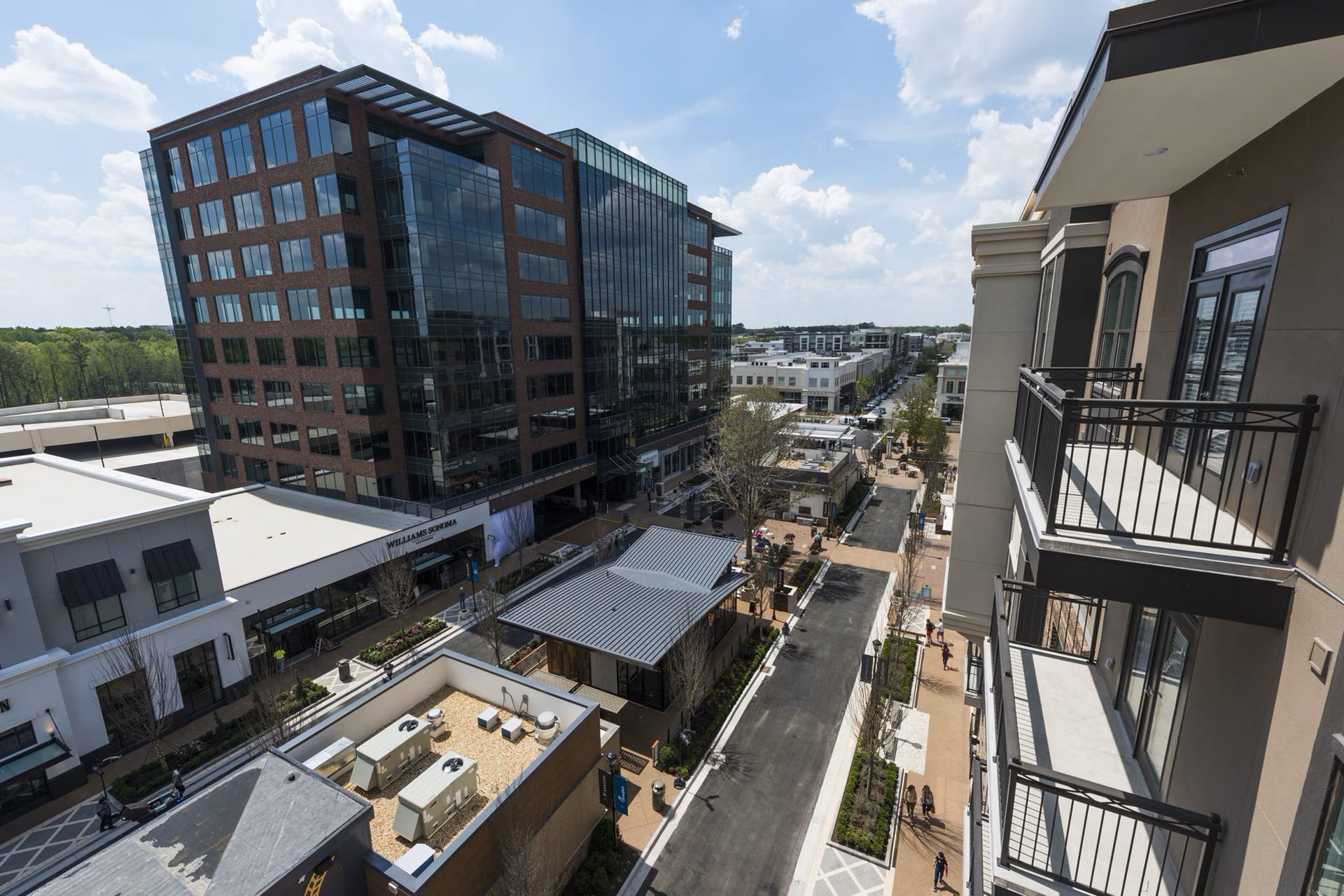 Cityscape with modern buildings, including a tall glass office building, shops, and a residential building with balconies.