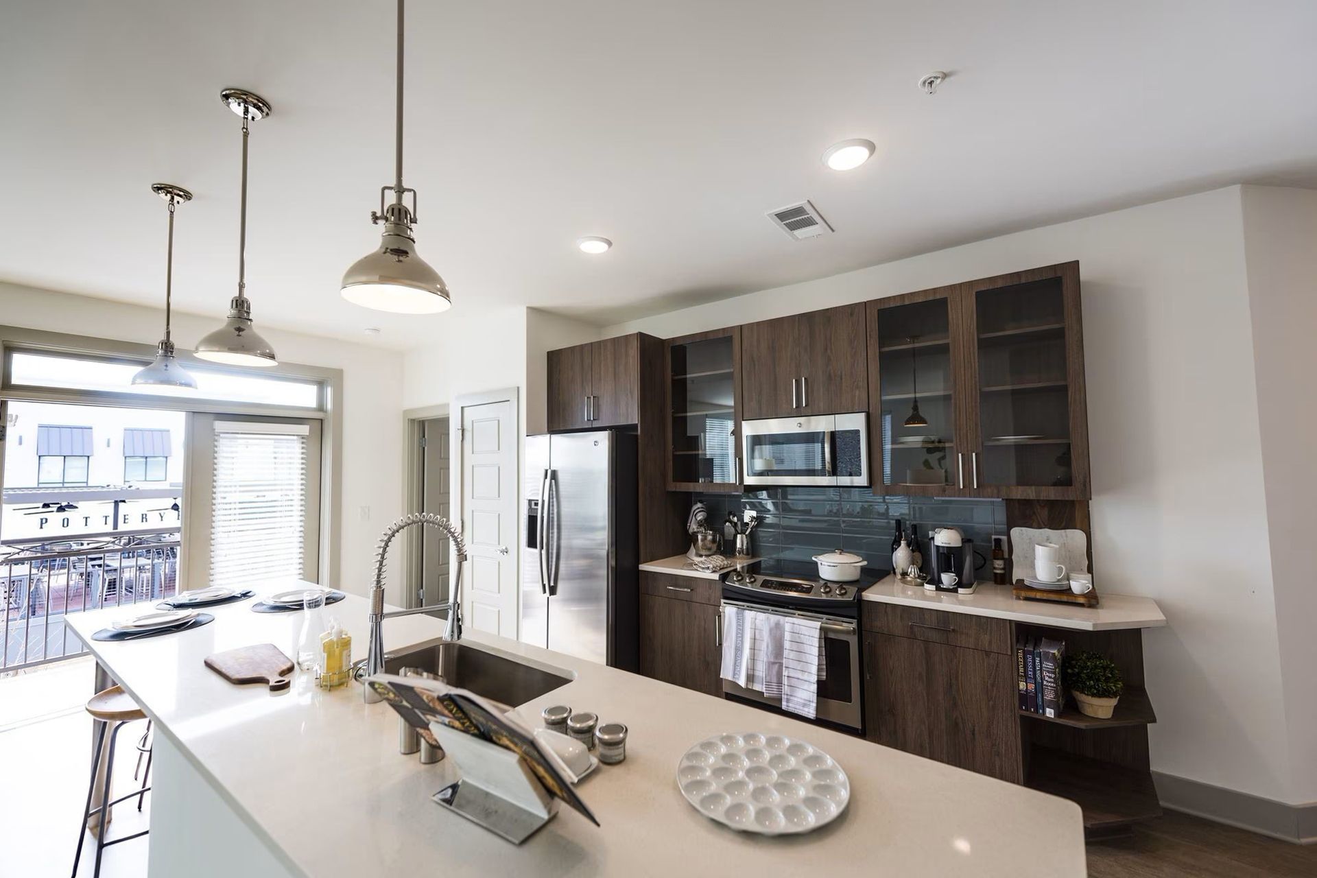 Modern kitchen with island, stainless steel appliances, dark wood cabinets, and a balcony view.