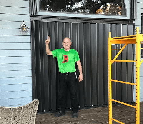 A man in a green shirt is standing in front of a garage door.