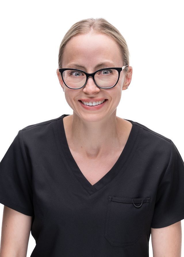Woman wearing glasses and black scrubs smiles.