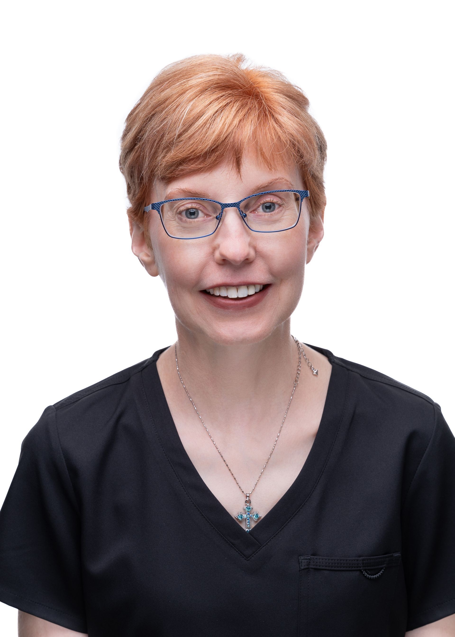 Woman with short red hair and glasses smiles. Wearing a black top and pendant necklace.