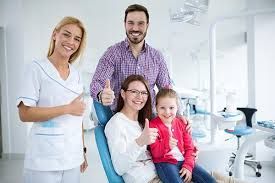 Family and dentist in dental office, smiling and giving thumbs up.