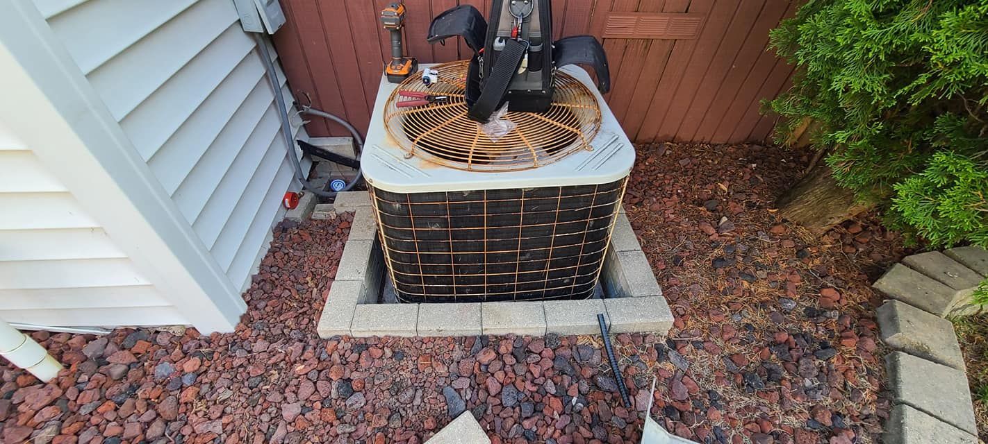 An air conditioner is sitting on top of a pile of gravel next to a house.