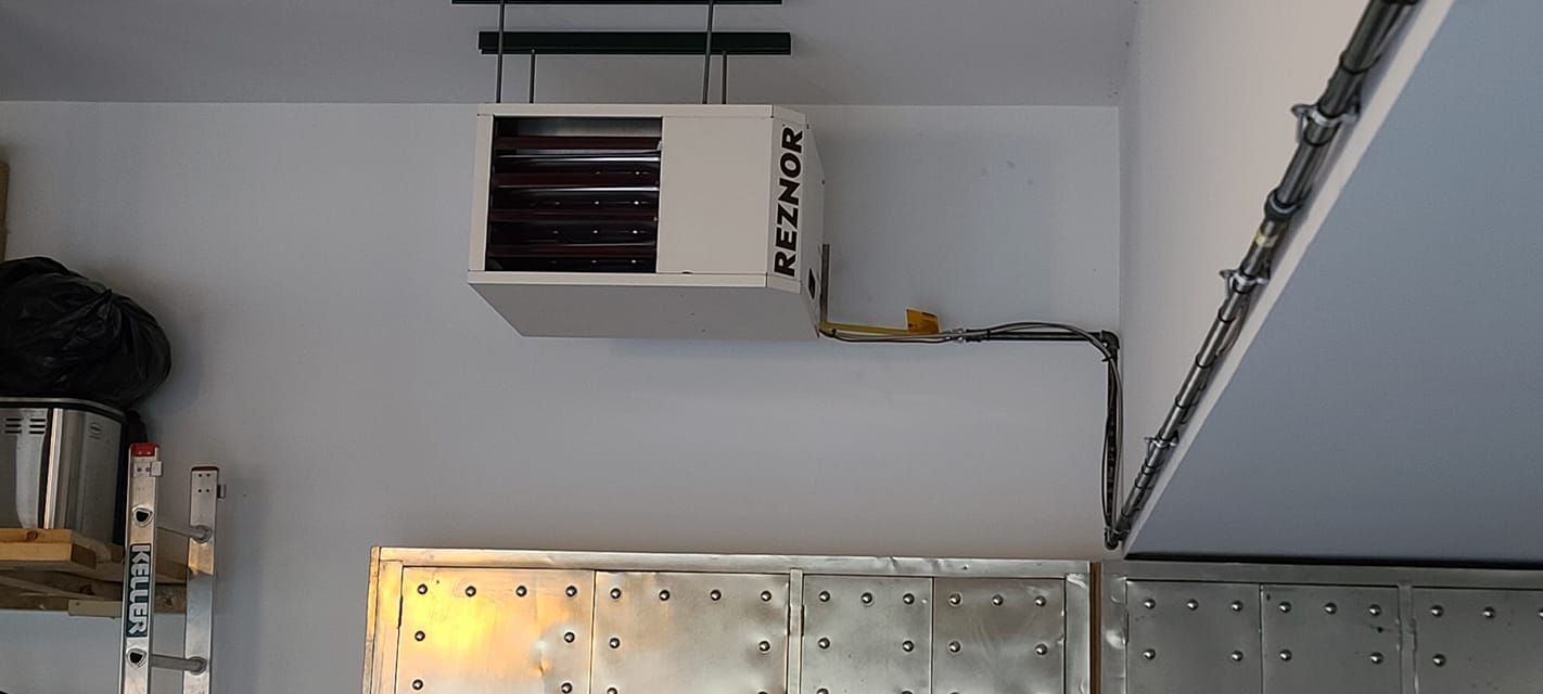 A heater is hanging from the ceiling of a garage.