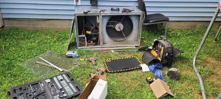An air conditioner is being repaired in a backyard.