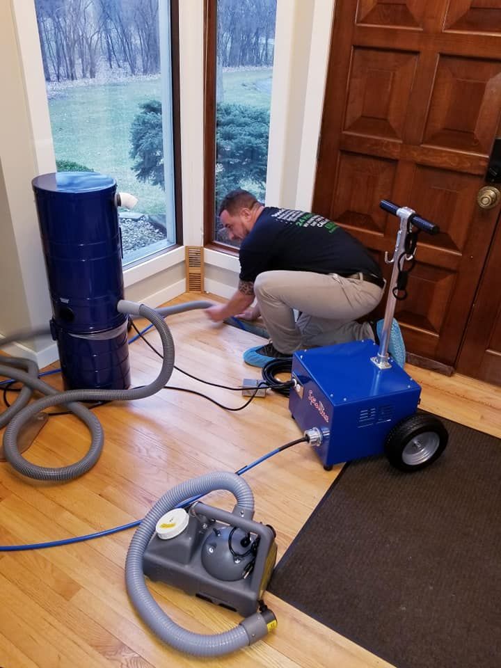 A man is kneeling on a wooden floor next to a vacuum cleaner.