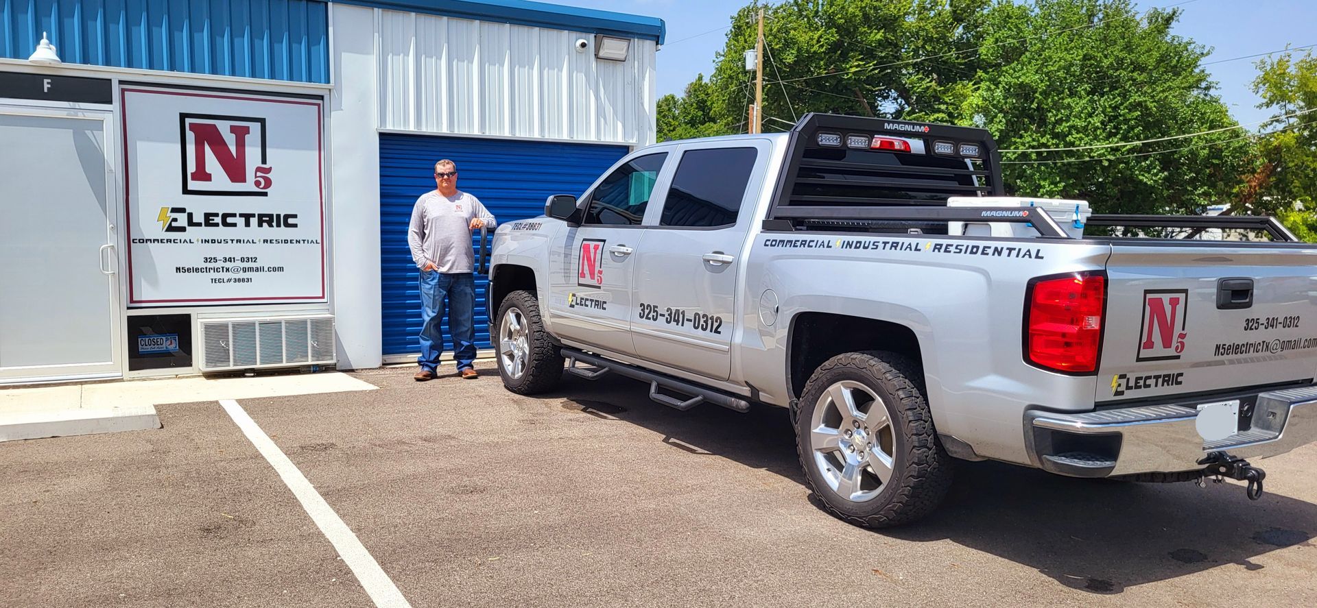 A man is standing next to a silver truck in a parking lot.
