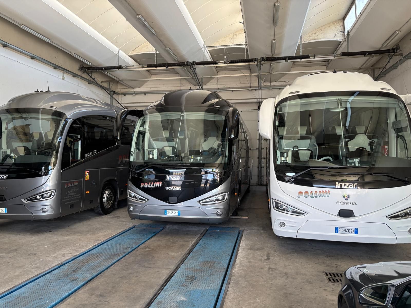 Tre autobus turistici parcheggiati in un garage. Sono visibili i colori grigio, nero e bianco.