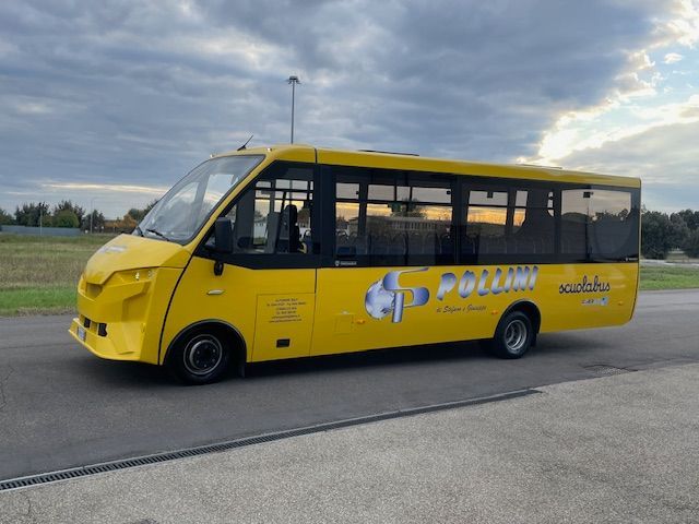 Autobus giallo parcheggiato su una superficie asfaltata con un marchio sul lato, sotto un cielo nuvoloso.