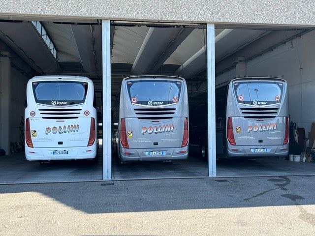 Tre autobus Pollini parcheggiati uno accanto all'altro sotto un'area coperta. Gli autobus sono grigi e bianchi.
