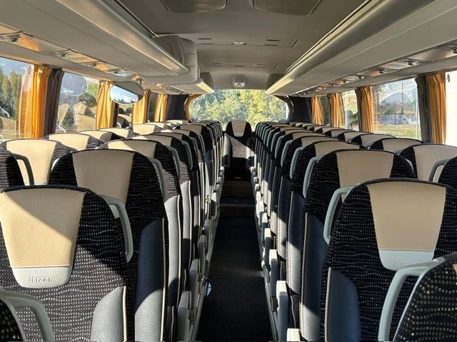 Vista interna di un autobus con file di sedili neri e color crema, finestrini con tendine su entrambi i lati.