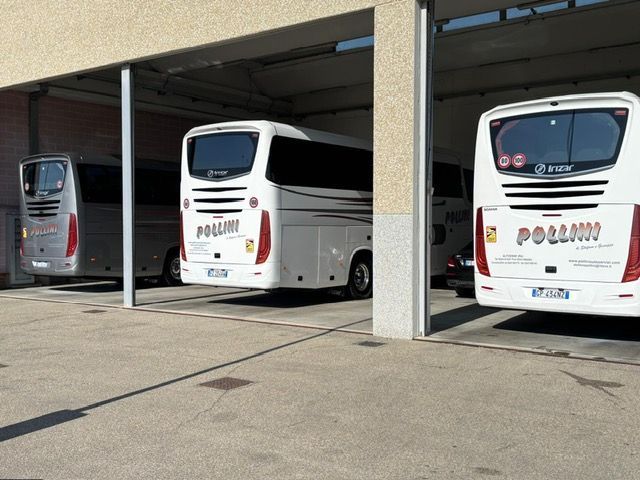 Tre autobus bianchi parcheggiati sotto una struttura coperta. Ogni autobus ha la scritta 