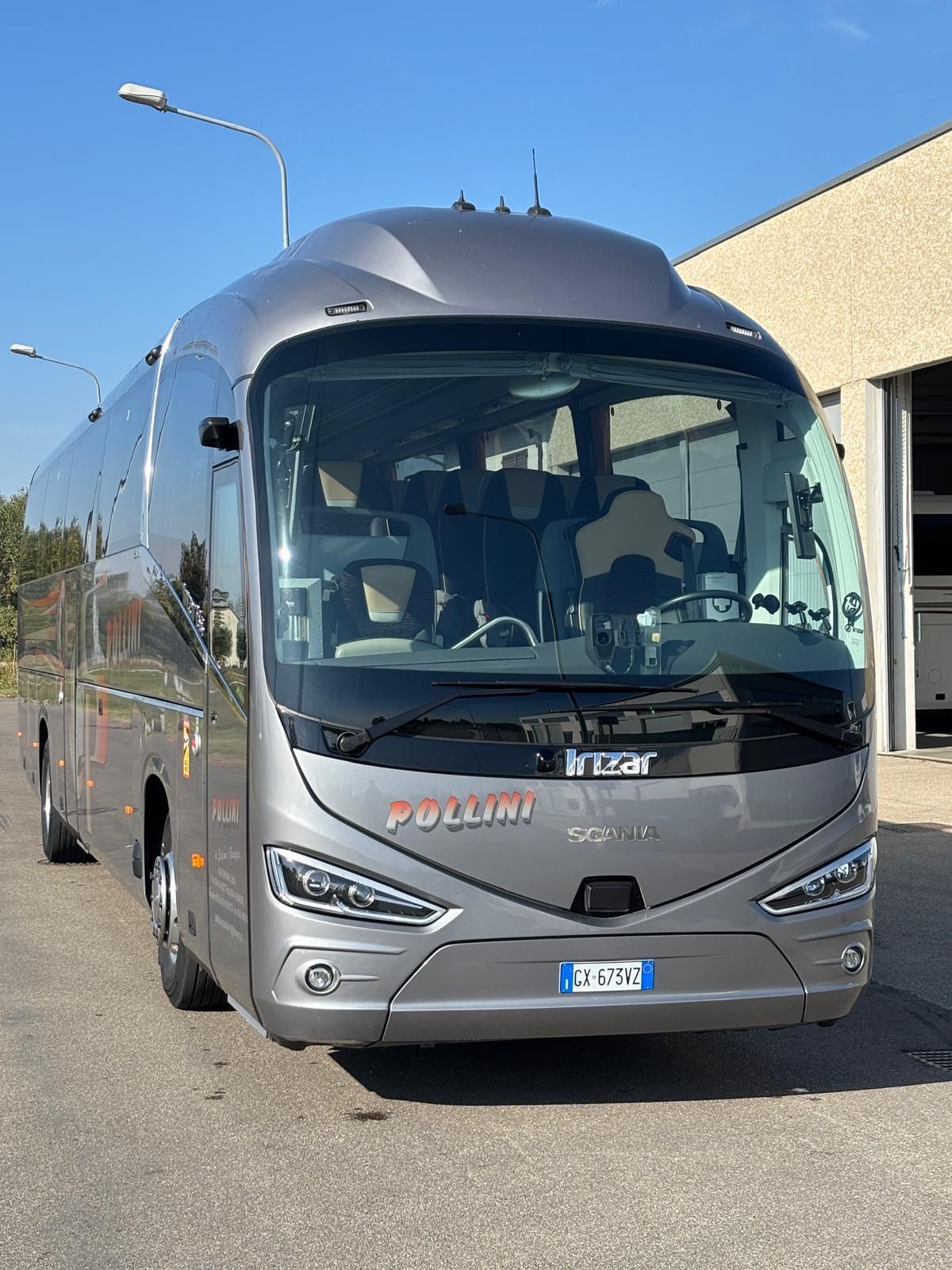 Un autobus turistico grigio parcheggiato davanti a un edificio in una giornata di sole.