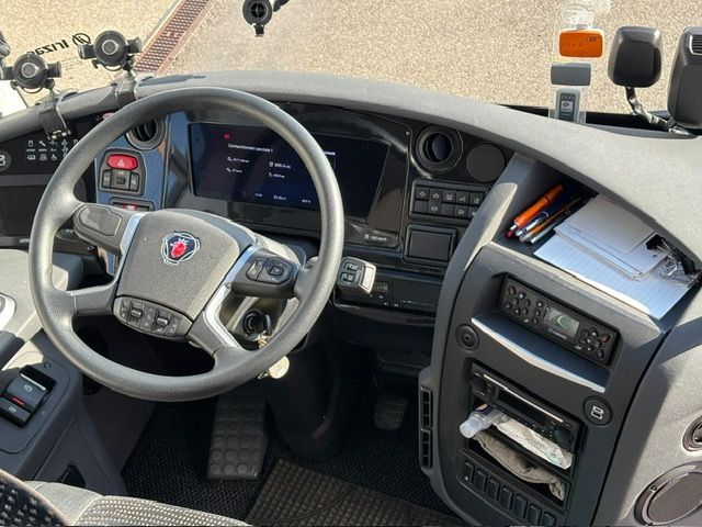 Interno della cabina di guida di un autobus Scania, in cui sono visibili il volante, il cruscotto con i comandi e il parabrezza.